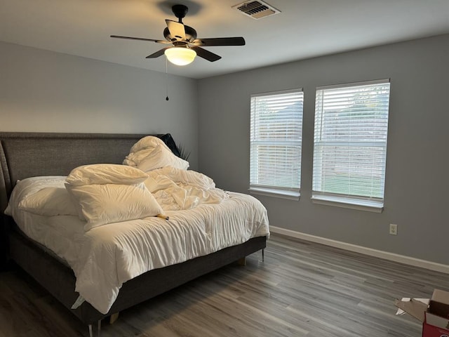 bedroom featuring baseboards, visible vents, multiple windows, and wood finished floors