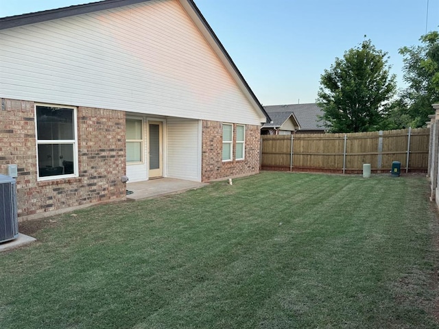 rear view of house with a yard, brick siding, central AC unit, and a fenced backyard