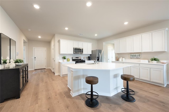 kitchen with light wood-style floors, white cabinetry, appliances with stainless steel finishes, and a center island with sink
