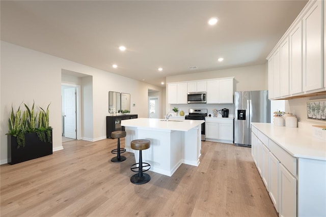 kitchen with white cabinets, appliances with stainless steel finishes, light wood-style floors, a breakfast bar area, and recessed lighting
