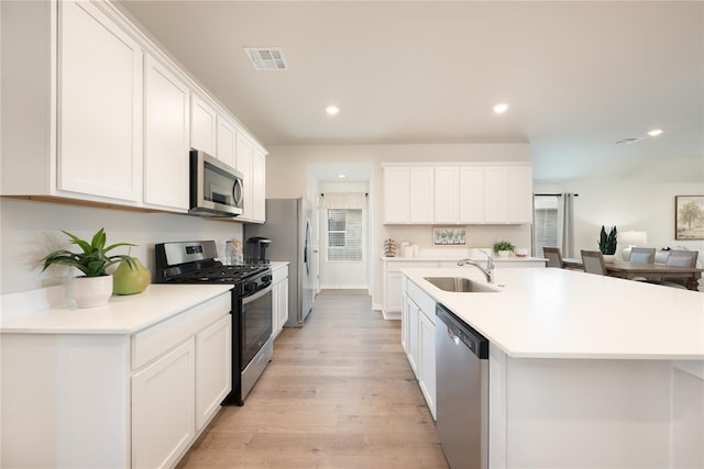 kitchen featuring visible vents, a center island with sink, white cabinetry, a sink, and stainless steel appliances