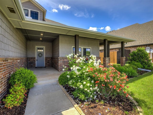 property entrance with fence, a porch, and brick siding