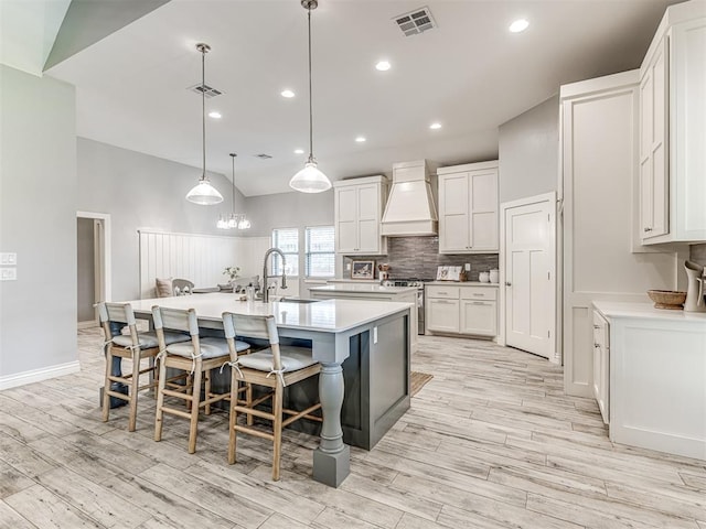 kitchen with a large island, visible vents, light wood-type flooring, a sink, and custom exhaust hood