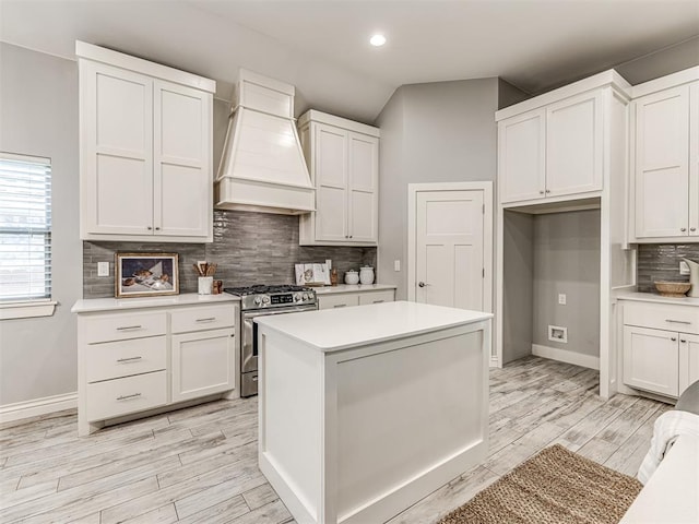 kitchen with stainless steel gas range oven, light countertops, white cabinets, custom range hood, and backsplash