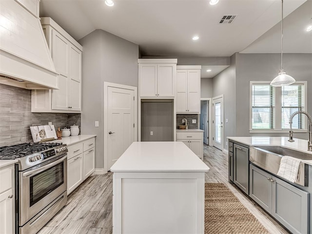 kitchen with decorative backsplash, a center island, a sink, stainless steel range with gas cooktop, and custom range hood