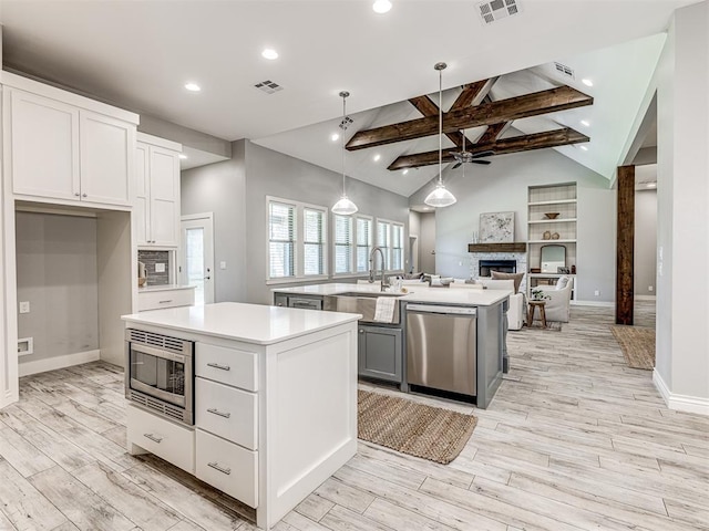kitchen with visible vents, a fireplace, a center island with sink, a sink, and stainless steel appliances