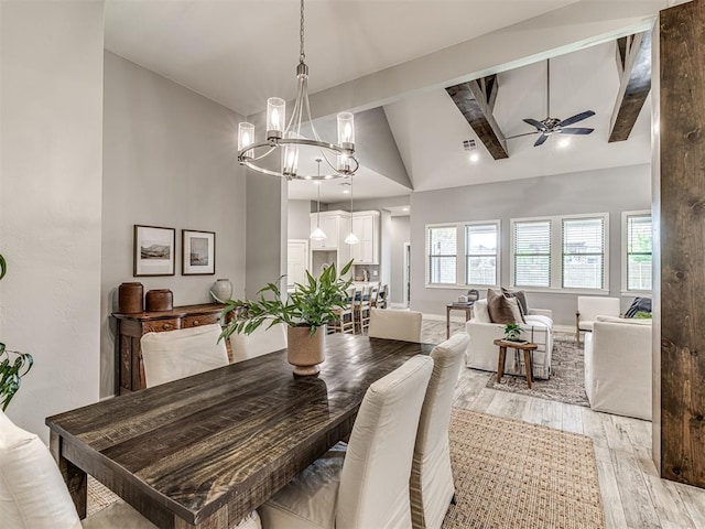 dining space with high vaulted ceiling, ceiling fan with notable chandelier, light wood-type flooring, beamed ceiling, and visible vents