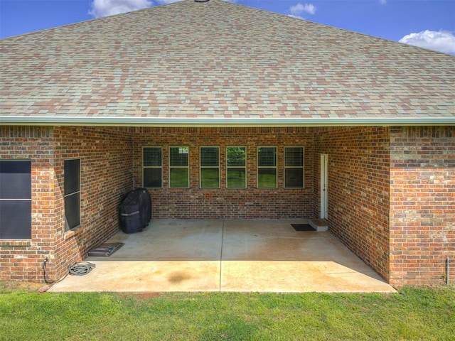back of house with brick siding, a shingled roof, and a patio area
