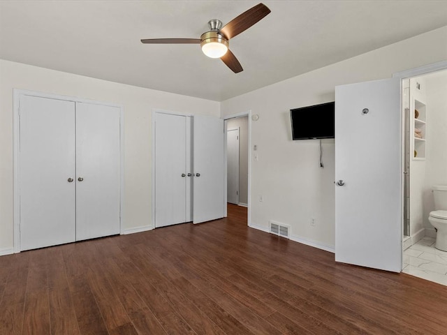 unfurnished bedroom with visible vents, wood finished floors, baseboards, two closets, and connected bathroom