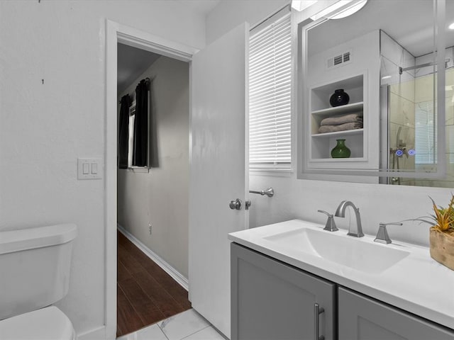 bathroom with a shower with shower door, vanity, toilet, baseboards, and visible vents