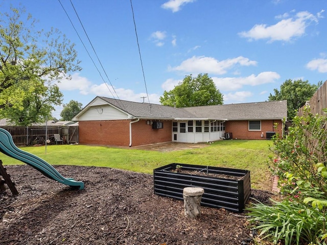 rear view of house with a playground, a yard, a fenced backyard, and brick siding