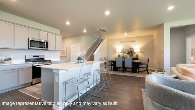 kitchen featuring light countertops, dark wood finished floors, an island with sink, stainless steel appliances, and visible vents