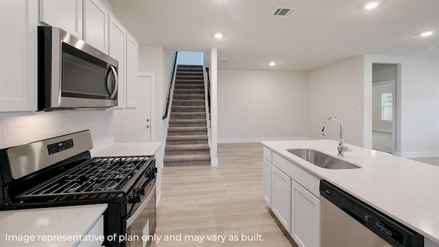 kitchen featuring visible vents, a sink, light stone counters, stainless steel appliances, and light wood-style flooring