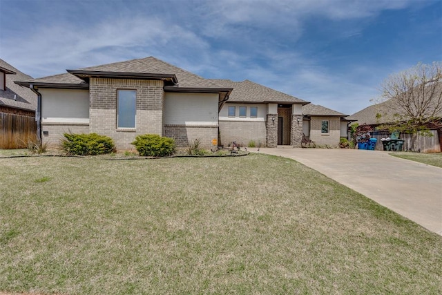 prairie-style home featuring a front lawn, fence, roof with shingles, brick siding, and driveway