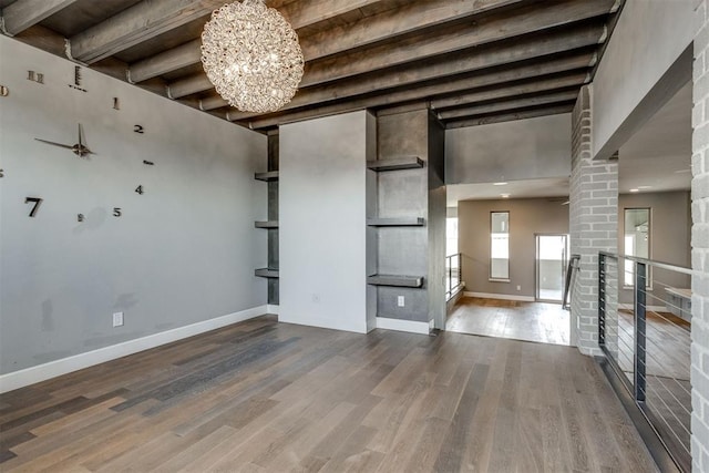 empty room with wood finished floors, baseboards, ceiling fan with notable chandelier, and beam ceiling