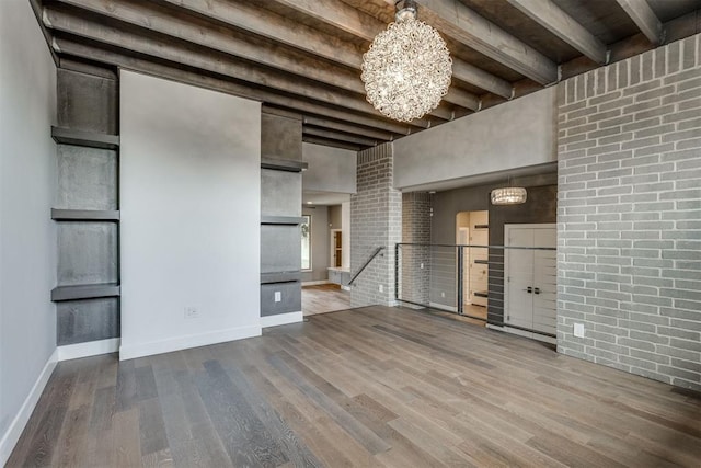 unfurnished living room with an inviting chandelier, a towering ceiling, wood finished floors, beamed ceiling, and baseboards