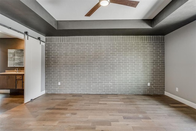unfurnished room featuring ceiling fan, wood finished floors, and brick wall