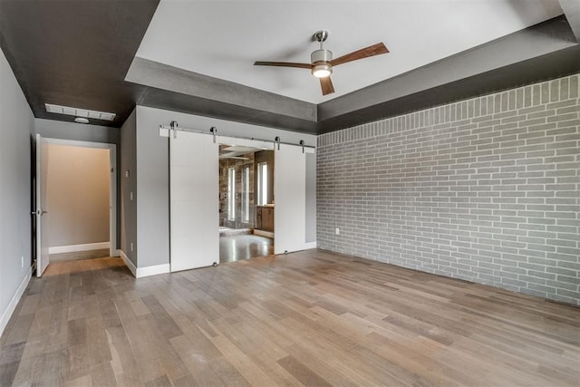 unfurnished room with baseboards, a barn door, a ceiling fan, and wood finished floors