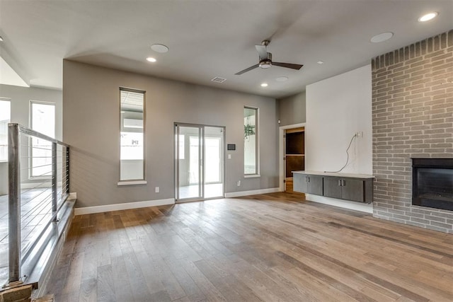 unfurnished living room with wood-type flooring, a ceiling fan, baseboards, and a healthy amount of sunlight