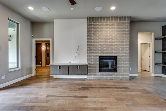 unfurnished living room featuring recessed lighting, baseboards, a fireplace, and light wood-type flooring