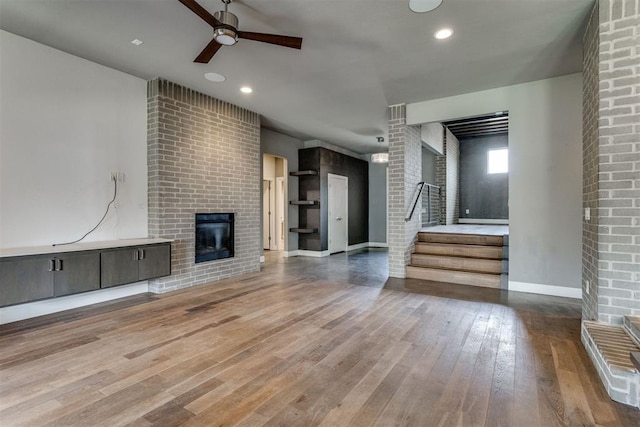 unfurnished living room featuring wood finished floors, a fireplace, baseboards, stairway, and a ceiling fan