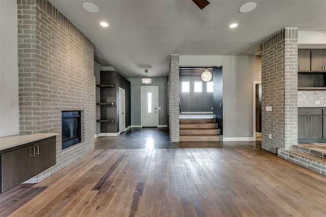 unfurnished living room with wood-type flooring, a brick fireplace, baseboards, stairway, and recessed lighting