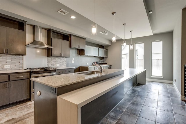 kitchen with visible vents, decorative backsplash, gas range, wall chimney exhaust hood, and a sink