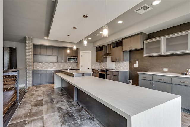 kitchen featuring a sink, stainless steel appliances, a large island with sink, backsplash, and visible vents