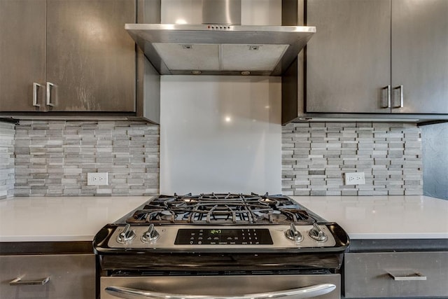 kitchen featuring dark brown cabinetry, backsplash, stainless steel gas range oven, light countertops, and wall chimney exhaust hood