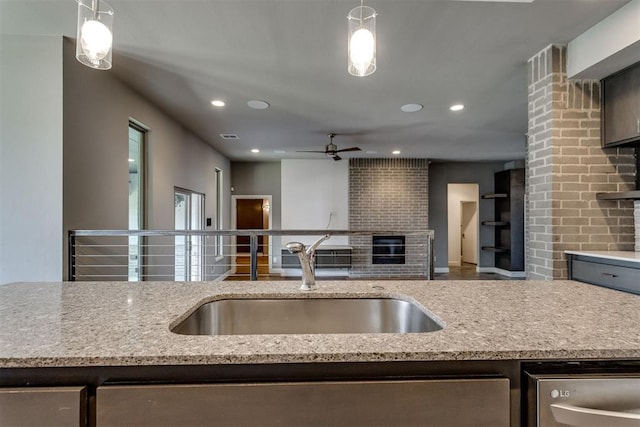 kitchen with a sink, a glass covered fireplace, recessed lighting, light stone counters, and a ceiling fan