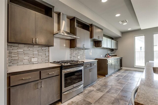 kitchen with wall chimney range hood, stainless steel range with gas cooktop, baseboards, backsplash, and visible vents