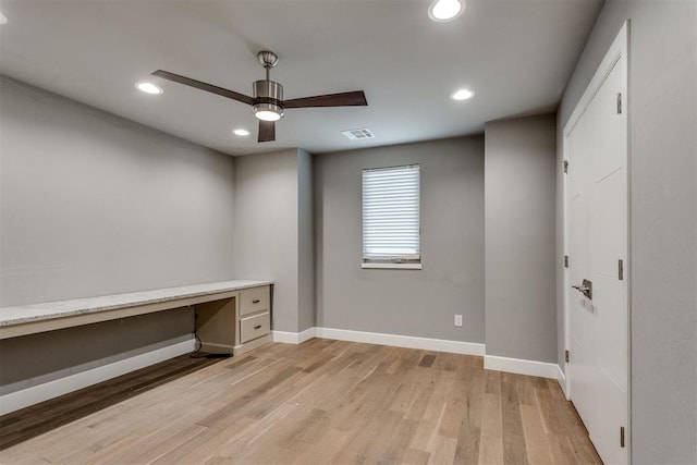 unfurnished office with built in study area, light wood-style flooring, a ceiling fan, baseboards, and visible vents