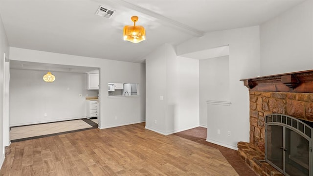 unfurnished living room featuring visible vents, a fireplace, light wood-style floors, baseboards, and vaulted ceiling with beams