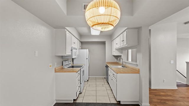 kitchen with a sink, light countertops, baseboards, a notable chandelier, and white appliances