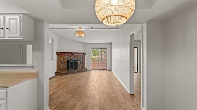 unfurnished living room with visible vents, light wood-style floors, baseboards, a stone fireplace, and a chandelier
