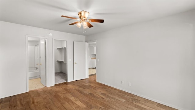 unfurnished bedroom featuring a walk in closet, a ceiling fan, wood finished floors, a closet, and ensuite bathroom
