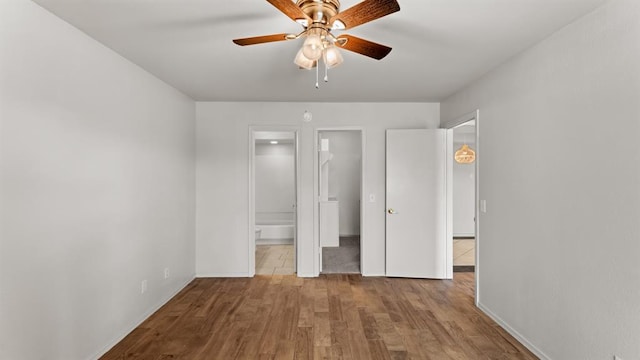 unfurnished bedroom featuring wood finished floors, baseboards, a closet, a spacious closet, and ensuite bath