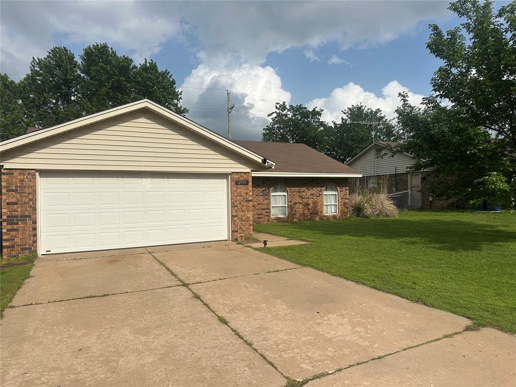2719 N Park Cir, Stillwater, OK 74075 - view of front of house with brick siding, a garage, driveway, and a front lawn