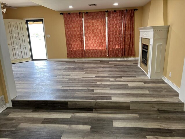 unfurnished living room with a glass covered fireplace, baseboards, recessed lighting, and wood finished floors