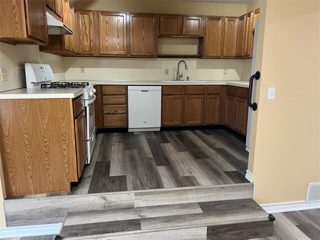 kitchen with a sink, light countertops, under cabinet range hood, white appliances, and dark wood-type flooring
