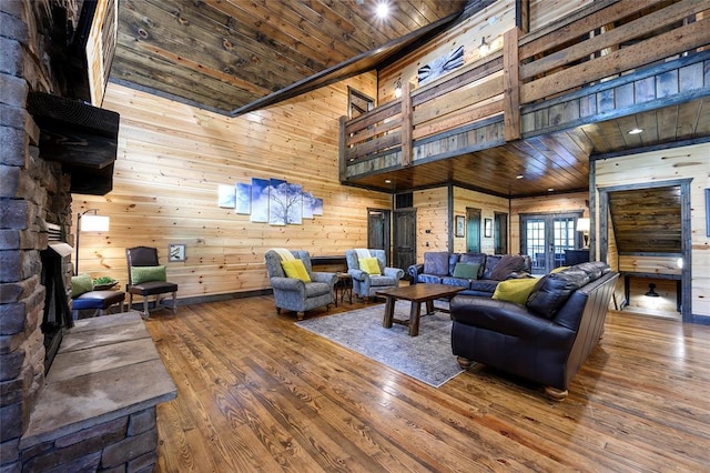living area with a fireplace, wood walls, wooden ceiling, a towering ceiling, and hardwood / wood-style flooring