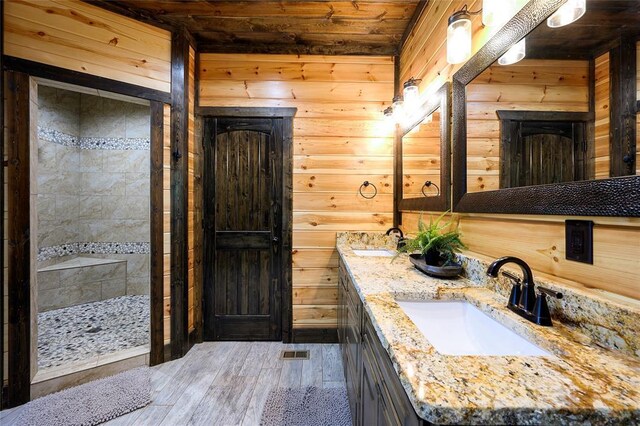 bathroom with wood walls, a tile shower, a sink, and hardwood / wood-style floors