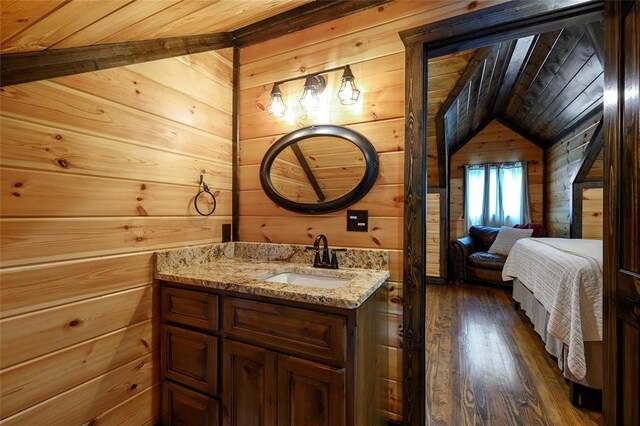 ensuite bathroom featuring vanity, wood-type flooring, wood walls, ensuite bathroom, and vaulted ceiling
