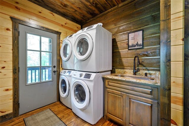 laundry area with stacked washer and dryer, wood walls, plenty of natural light, and a sink
