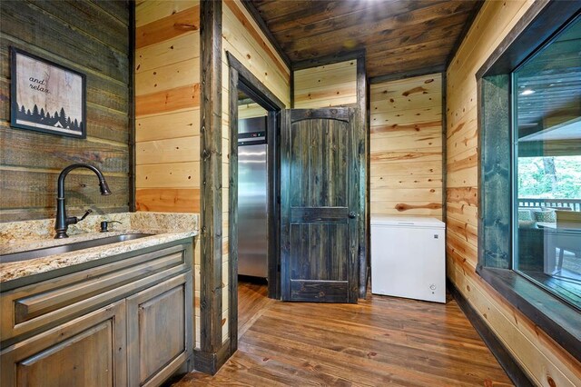 kitchen with light stone countertops, wooden walls, dark wood-style floors, wood ceiling, and a sink