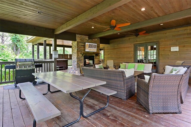 wooden terrace featuring french doors, area for grilling, a ceiling fan, an outdoor living space with a fireplace, and outdoor dining space