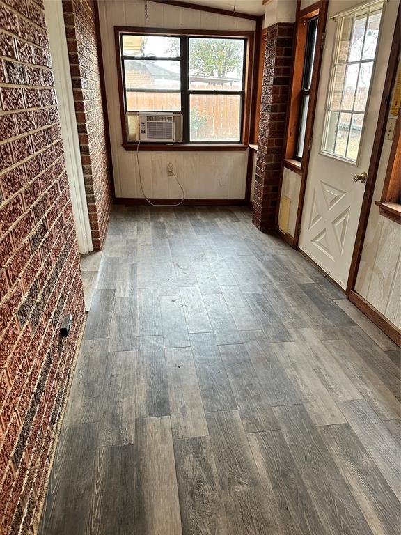spare room featuring brick wall, baseboards, cooling unit, and wood finished floors