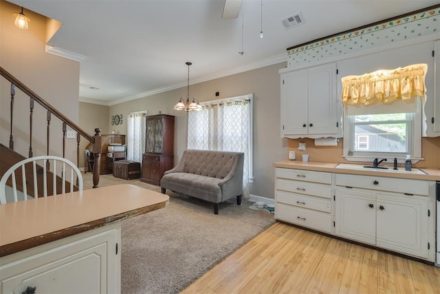 kitchen with visible vents, ornamental molding, white cabinets, a sink, and light wood-style flooring