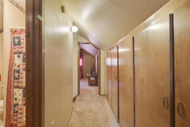 hallway with a textured ceiling, a textured wall, lofted ceiling, and light carpet