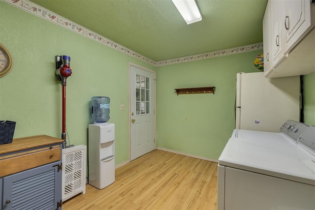 washroom featuring a textured ceiling, cabinet space, baseboards, light wood-style flooring, and washer and clothes dryer